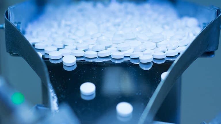 White pharmaceutical pills being sorted on a conveyor belt in a manufacturing facility, representing process safety in drug production.