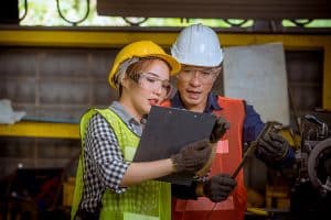 Two engineers in safety helmets and protective gear reviewing a checklist during a Pre-Startup Safety Review (PSSR) in an industrial facility.