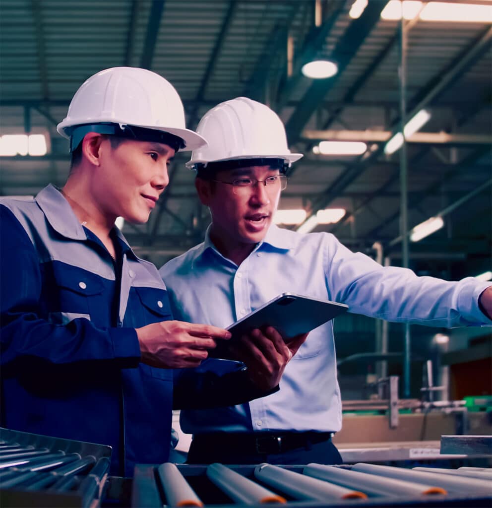 Two engineers wearing safety helmets and holding clipboards, collaborating on a Hazard and Operability (HAZOP) study in an industrial facility to identify risks and enhance safety measures.