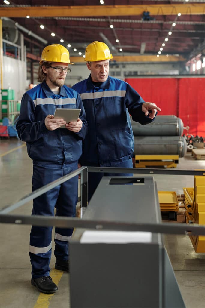 Two engineers in safety helmets conducting hazard identification review in an industrial facility