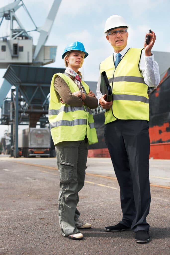 Two engineers in safety vests and helmets conducting a process safety review at an industrial site during a HAZOP study